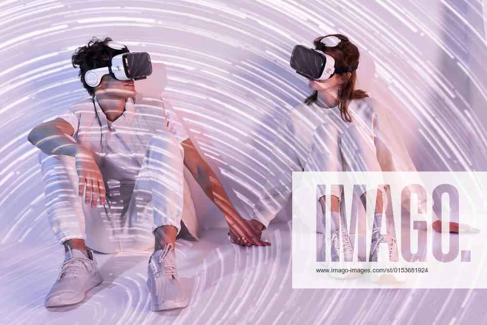 IMAGO Creative: Business, Innovative Technologie-L?sungen Full body of couple in modern VR goggles exploring virtual reality while sitting at wall holding hands with long exposure lights in studio ManuelRuiz_VRCouple_4.jpg