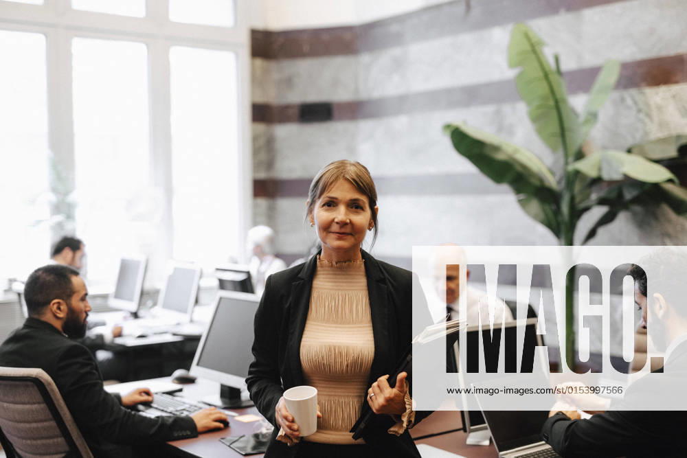 IMAGO Creative: Business, Innovative Technologie-Lösungen Portrait of smiling mature female leader holding coffee cup and documents at law office Sweden, Stockholm, model released, property released