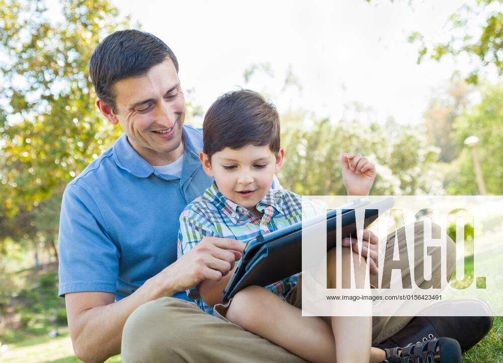 Happy father and son playing on a computer tablet outside