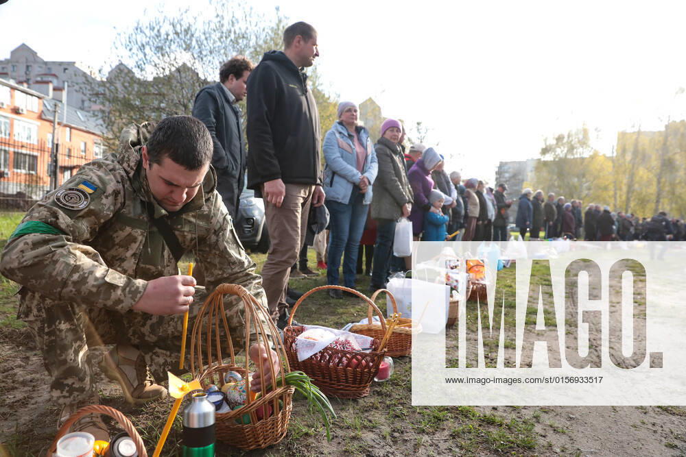 BUCHA, UKRAINE - APRIL 24, 2022 - A serviceman sits on his haunches near an Easter basket before a consecration ceremony outside the Church of Saint Andrew the First-Called Apostle during the Orthodox Easter celebration in Bucha that is recovering from the war crimes committed by Russian troops after its liberation from Russian invaders, Kyiv Region, northern Ukraine. Easter service in Bucha