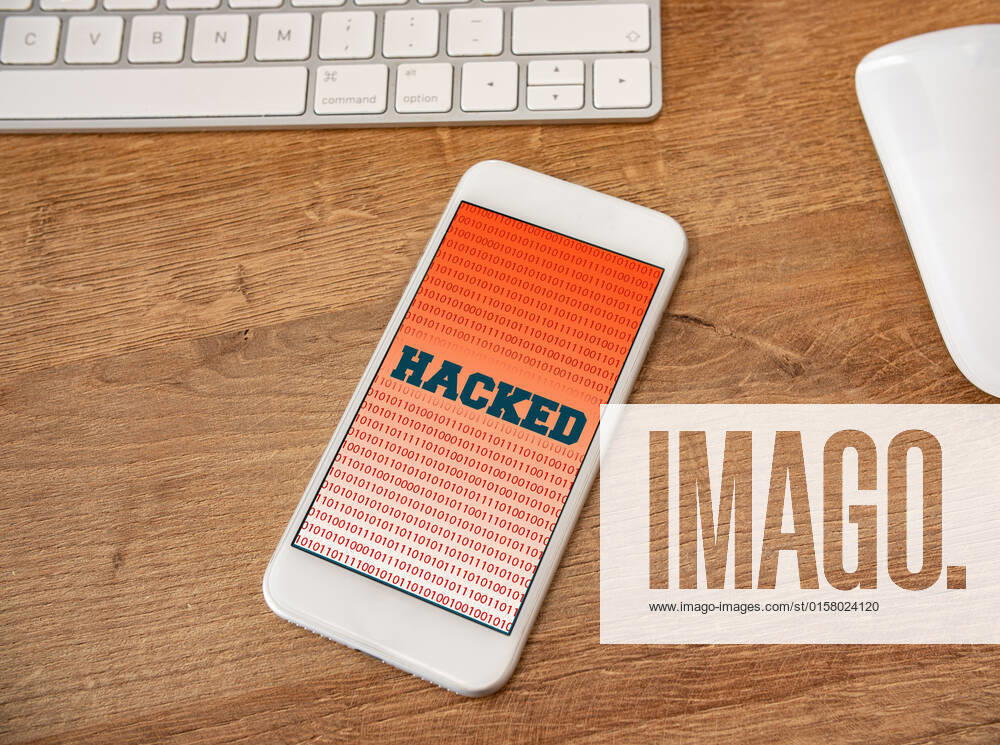 A hacked mobile phone on a desk. Mobile phone on a desk surrounded by a keyboard and computer mouse. The screen from the mobile device shows the word hacked. Mobile security, Internet crime and mobile device hacking concept.