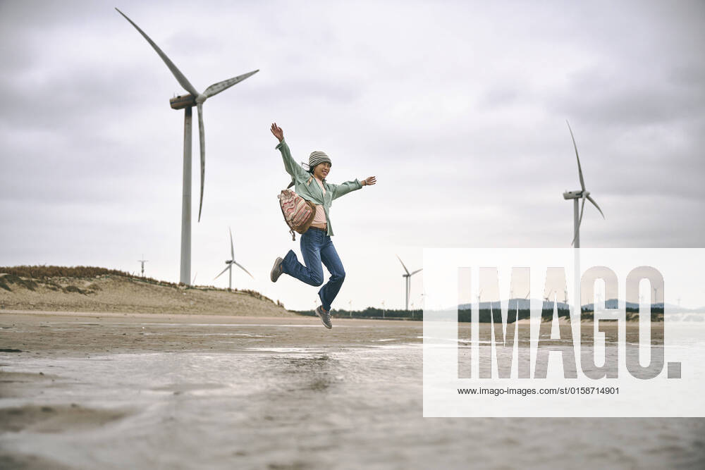 IMAGO Creative: N?chste Generation, Sozial- und klimabewusst Side view of young female in casual clothes with backpack jumping on seaside near windmills on cloudy day LuisGomez_ChristinaOnTheBeach_3.jpg
