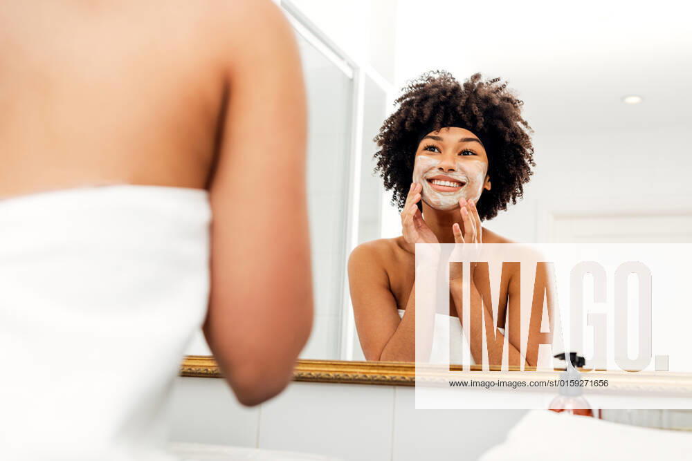 Woman applying facial mask in front of bathroom mirror