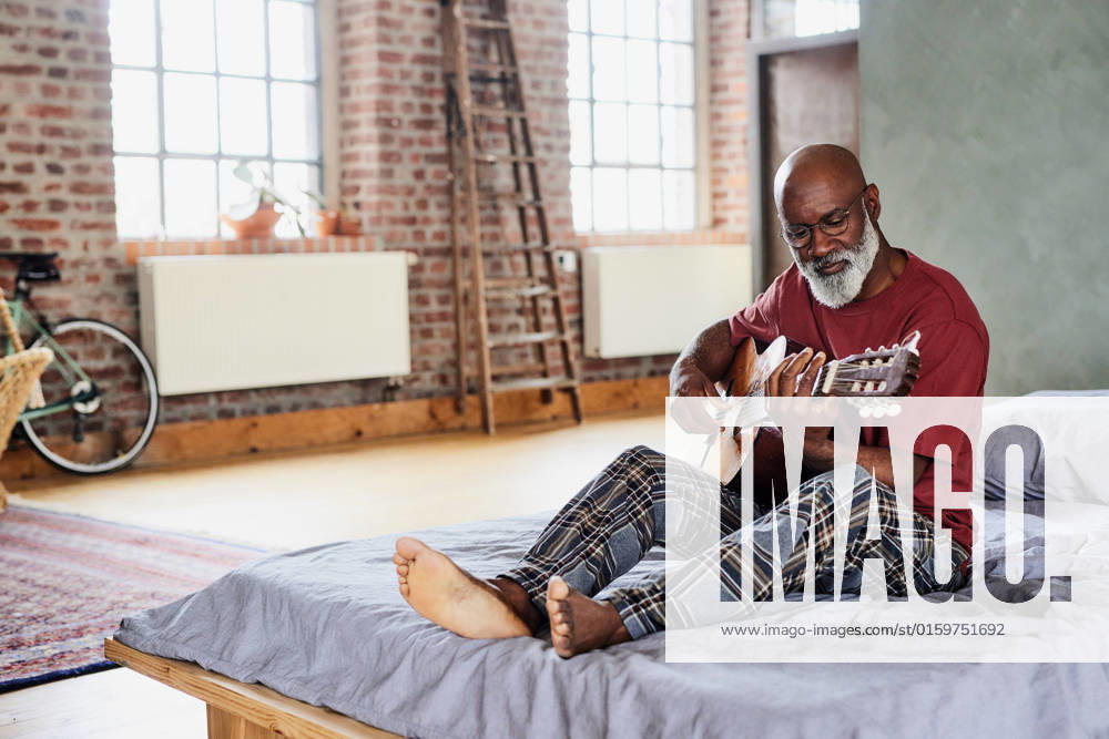 Man with eyeglasses playing guitar on bed at home model released, Symbolfoto property released, FMKF07456