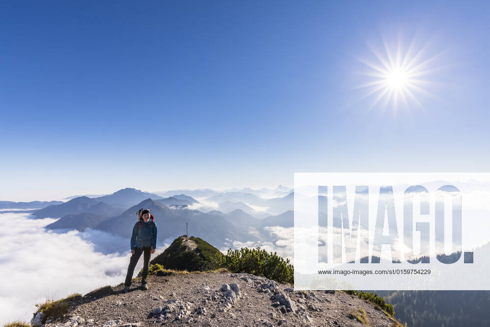 Germany, Bavaria, Sun shining over female hiker standing on mountaintop with thick fog and peak of Herzogstand mountain in background model released, Symbolfoto, FOF13153