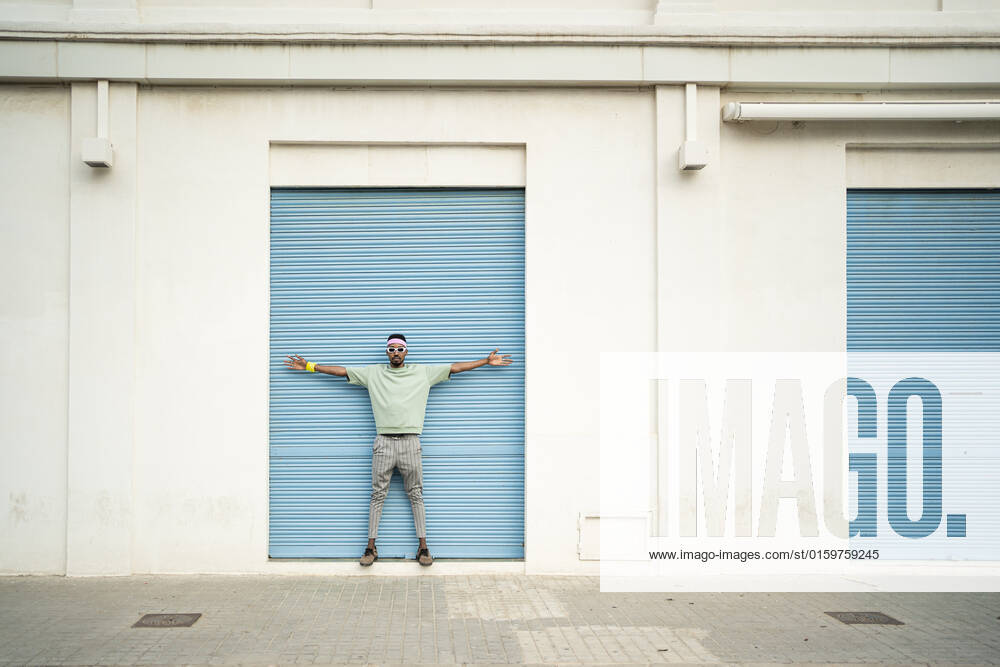 Young man standing with arms outstretched in front of blue shutter model released, Symbolfoto, RCPF01453