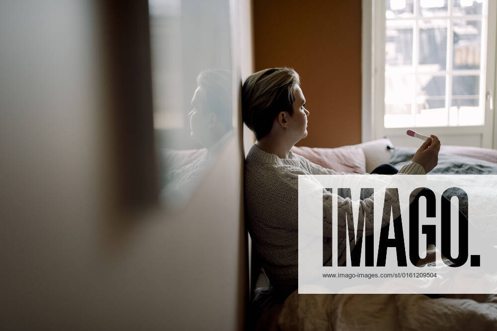 IMAGO Creative: 2022 Favoriten Side view of upset woman holding pregnancy test result sitting on bed at home Sweden, Stockholm, model released, property released