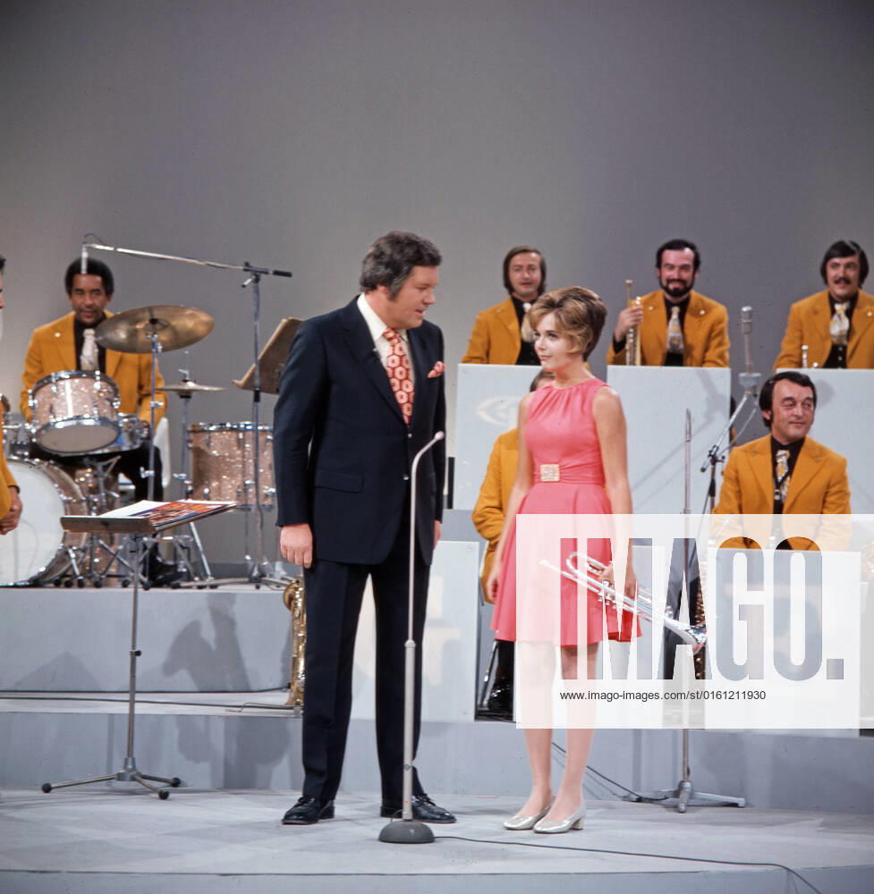 DREI MAL NEUN Drei mal Neun, ZDF Quizshow, Deutschland, 1971, im Bild: Showmaster Wim Thoelke im Gespräch mit der amerikanischen Trompetensolistin Carole Dawn Reinhart, im Hintergrund: Musiker der Max Greger Bigband. Drei mal Neun, TV quiz show, Germany, 1971, on the photo: presenter Wim Thoelke talks with American trumpet soloist Carole Dawn Reinhart, in the background: musicians from the Max Greger Big Band., Deutschland