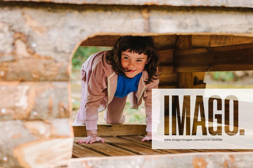 Full body of curious adorable little girl with dark hair in casual wear smiling and looking away while climbing into small wooden house on playground, Model released HodeiUnzueta_HangingParkAmongTrees_25.jpg