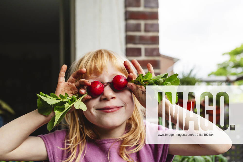 IMAGO Creative, Sommer, Food, Radieschen Smiling girl covering eyes with fresh radish on balcony model released, Symbolfoto property released, IHF00833