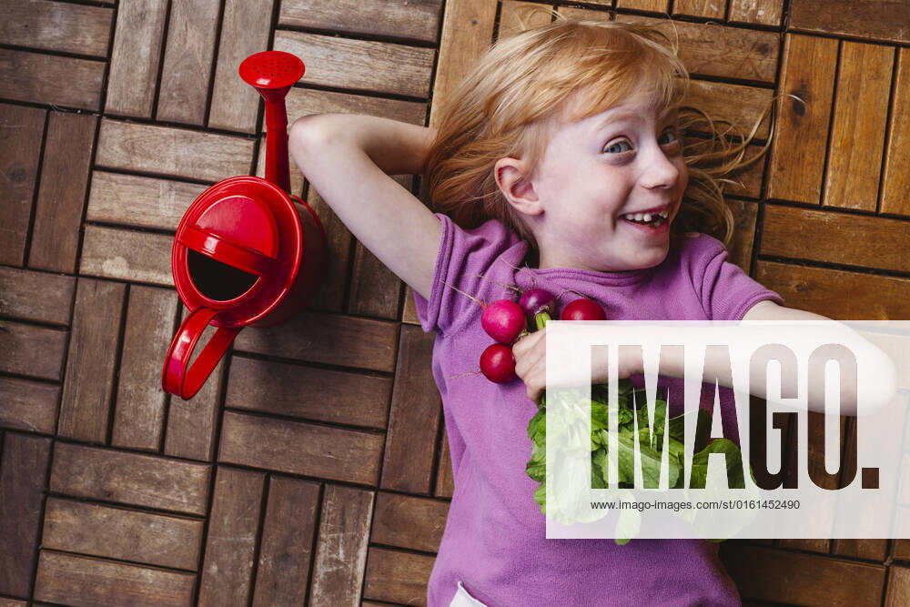 IMAGO Creative, Sommer, Food, Radieschen Happy girl with radish lying by watering can on balcony floor model released, Symbolfoto property released, IHF00839