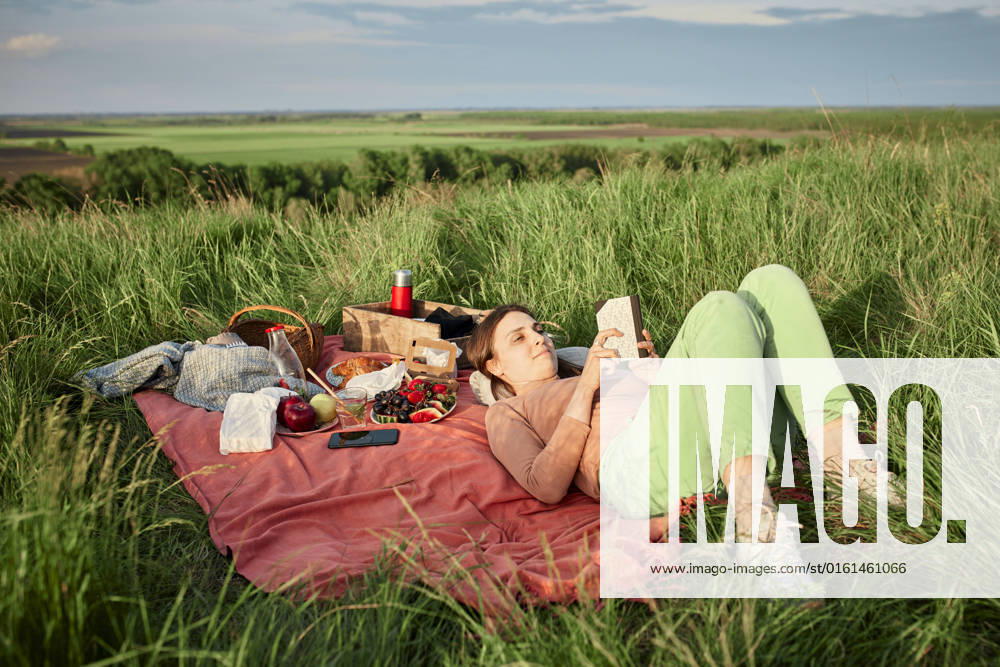 Smiling woman reading book at picnic in field model released, Symbolfoto, ZEDF04592
