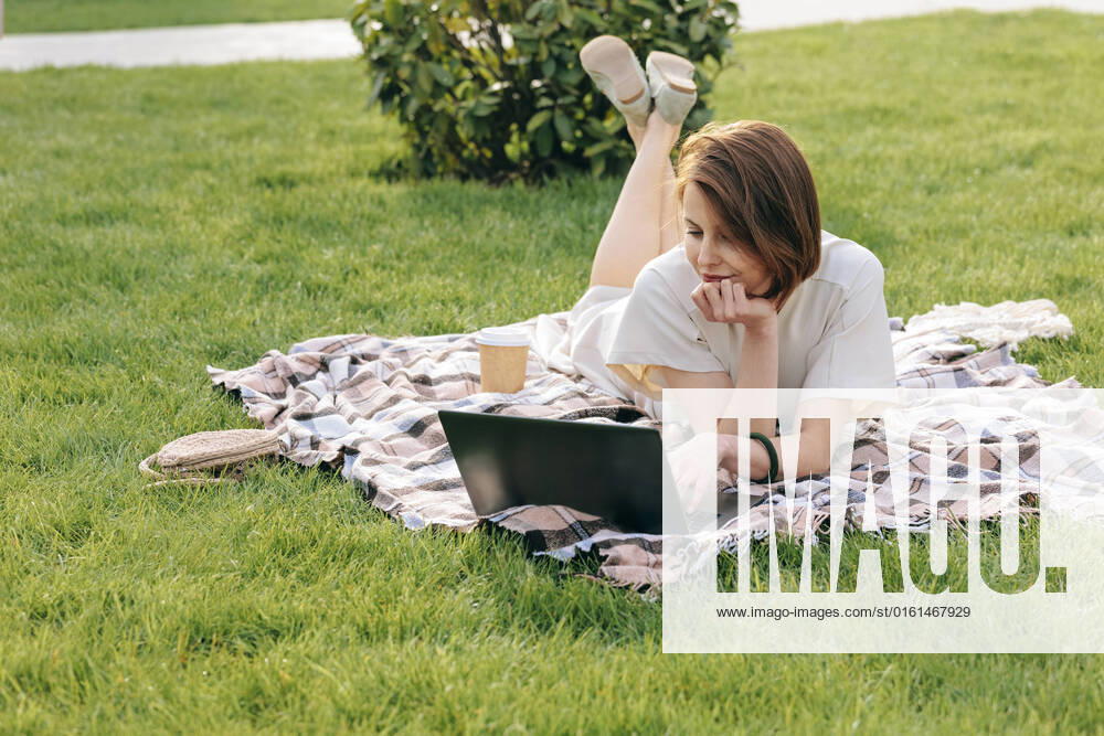 Woman with laptop lying on picnic blanket at park model released, Symbolfoto, OMIF00823