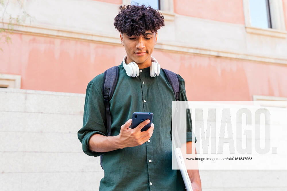 IMAGO Creative: N?chste Generation, Sozial- und klimabewusst Ethnic man with headphones looking at screen of modern mobile phone on the street DavidMunoz_FrancVilaOlimpica_00009.jpg