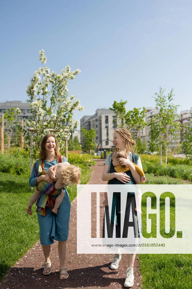 IMAGO Creative: Sommer, Sommertage im Stadtpark Full length of smiling Caucasian mothers carrying their babies in slings at park on sunny day, Model released LiliyaSolopova_MumsWithBabiesOutdoors_00016.jpg