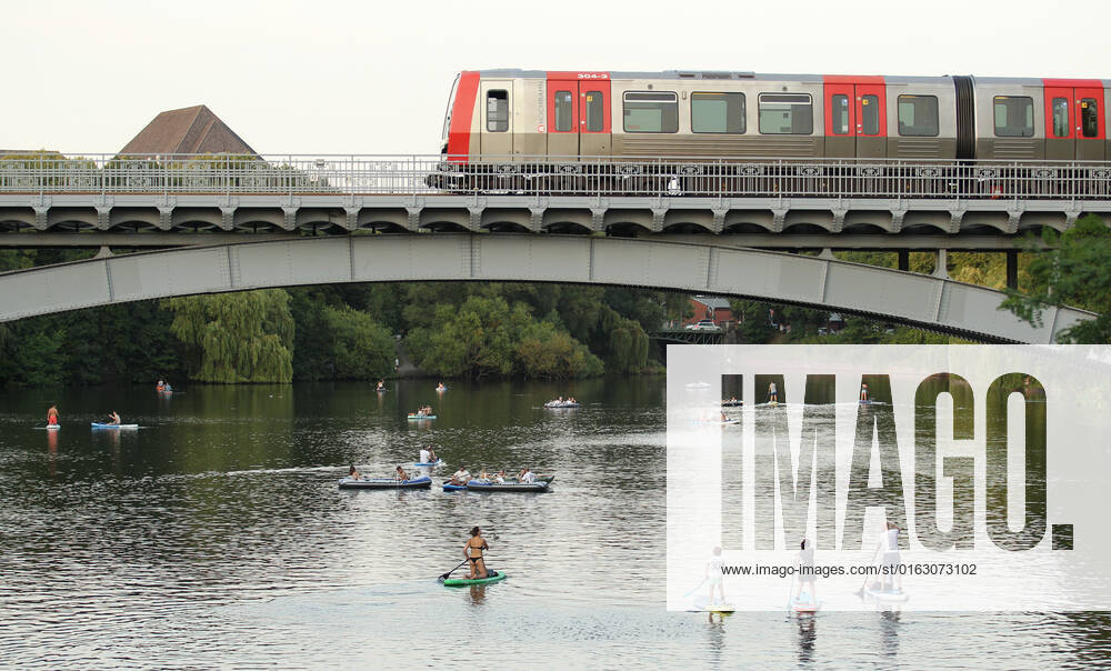 Passers-by paddle on stand up paddle boards along an Alster canal under a bridge, which is just crossed by a subway On Tuesday evening, temperatures in Hamburg were still up to 30 degrees until late in the evening Hohenfelde Hamburg