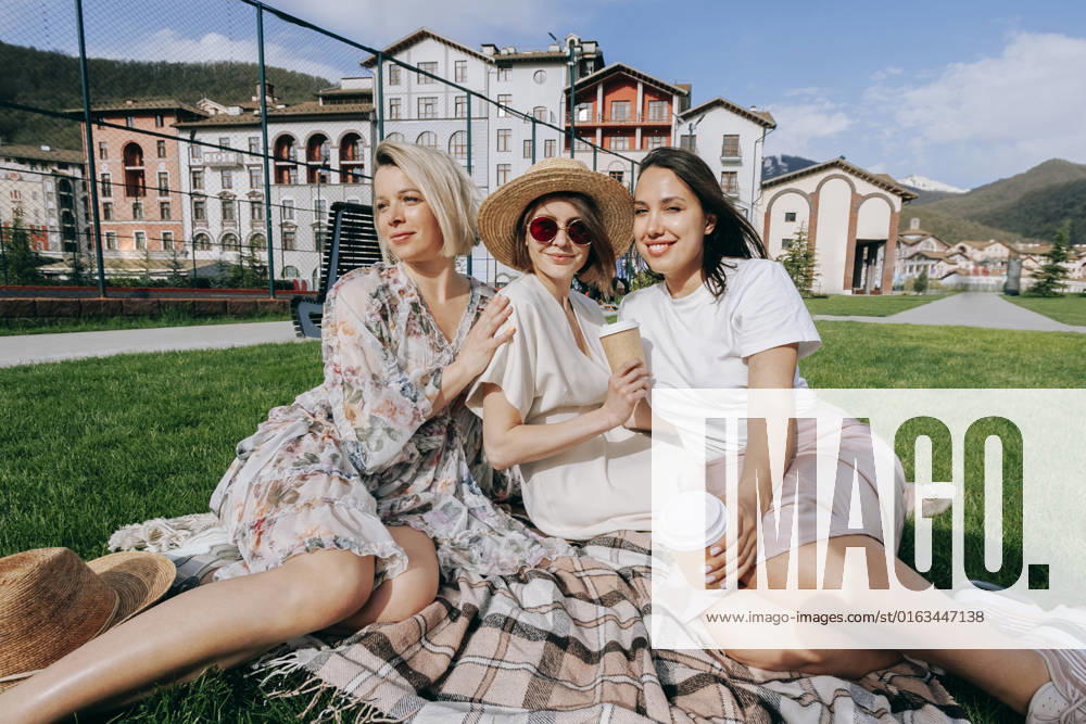 IMAGO Creative: Sommer, Sommertage im Stadtpark Smiling women with disposable coffee cups sitting on picnic blanket at park model released, Symbolfoto, OMIF00871