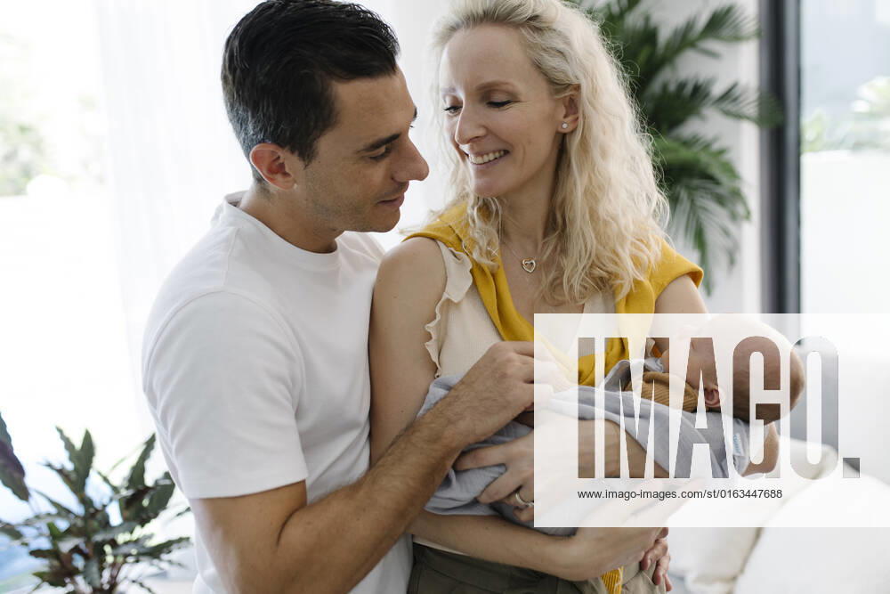 Smiling woman carrying baby in arm sitting by man at home model released, Symbolfoto property released, TYF00249