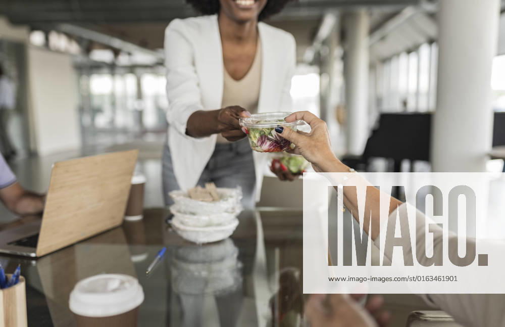 Businesswoman giving salad box to senior colleague at desk model released, Symbolfoto property released, JCICF00179