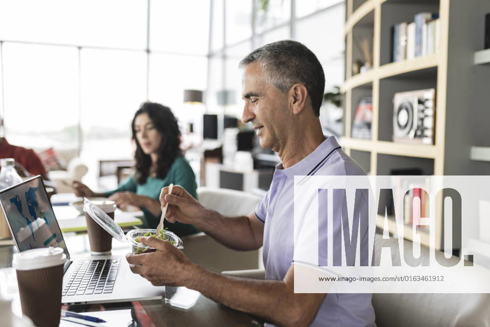 Happy businessman eating salad at desk in office model released, Symbolfoto property released, JCICF00188