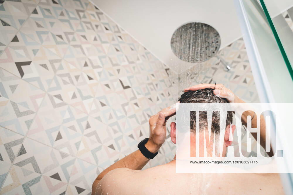 attractive young man takes a shower under running water in the shower in the bathroom, body care with shampoo