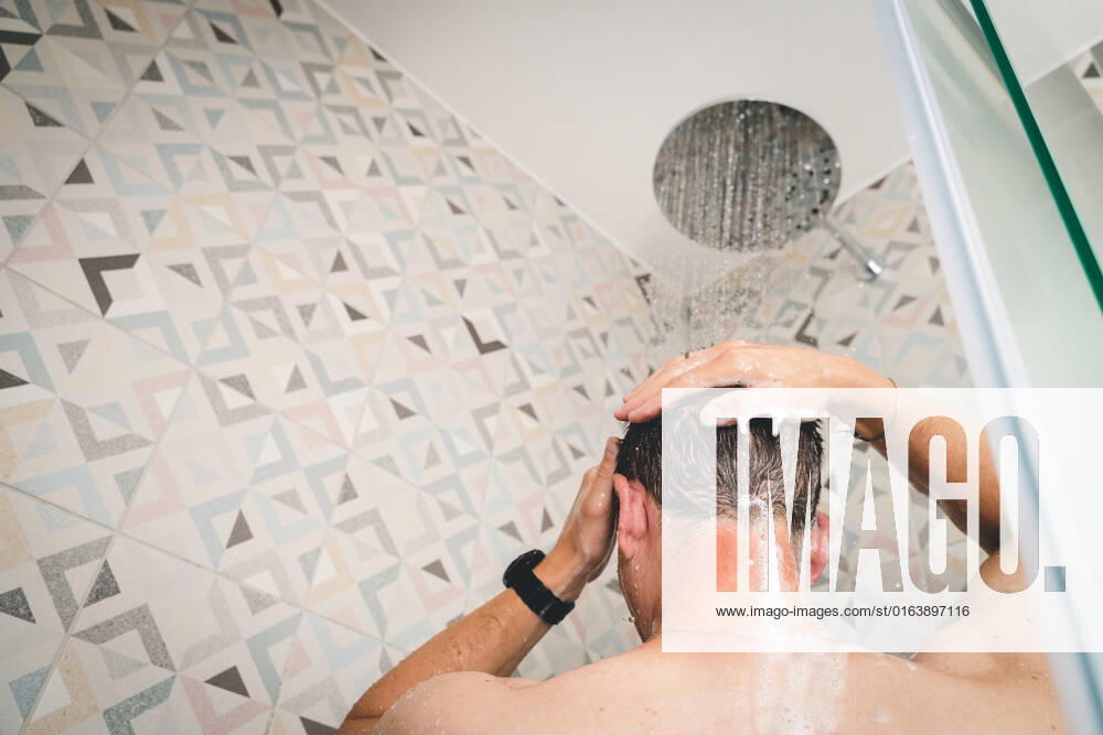 attractive young man takes a shower under running water in the shower in the bathroom, body care with shampoo