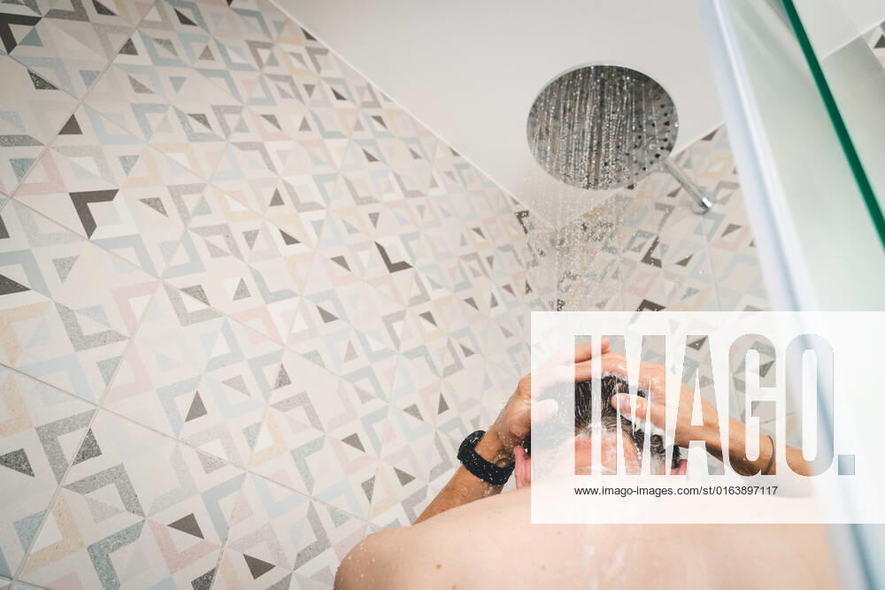 attractive young man takes a shower under running water in the shower in the bathroom, body care with shampoo