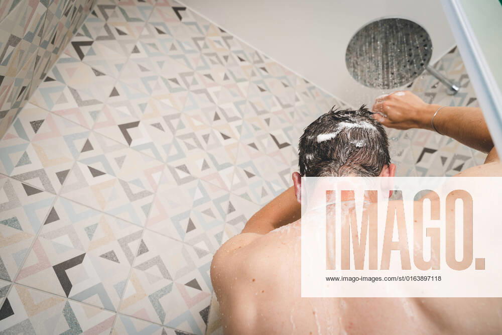 attractive young man takes a shower under running water in the shower in the bathroom, body care with shampoo