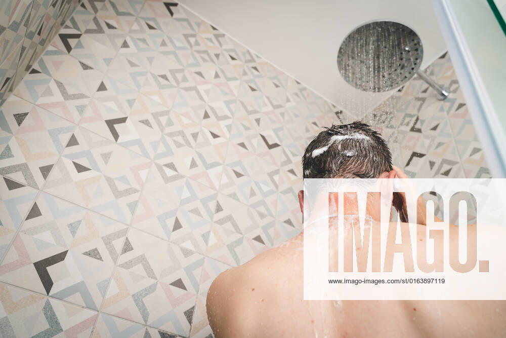 attractive young man takes a shower under running water in the shower in the bathroom, body care with shampoo