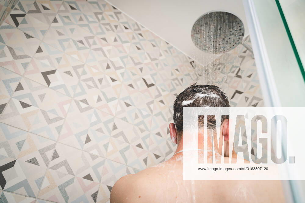 attractive young man takes a shower under running water in the shower in the bathroom, body care with shampoo