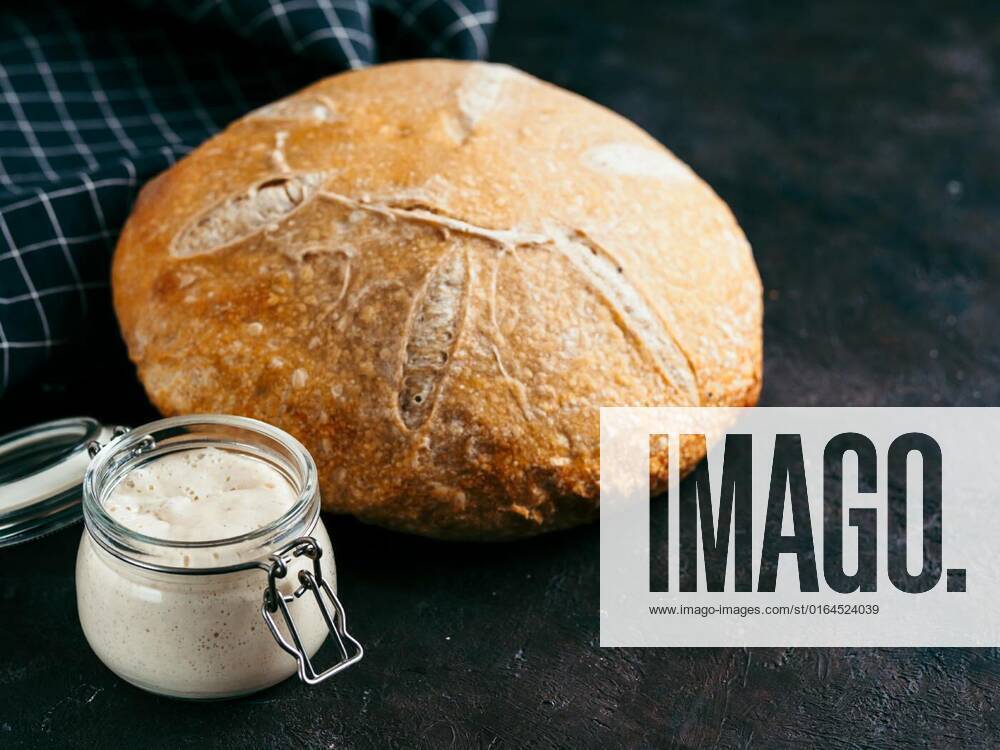 Sourdoug starter and wheat bread, copy space, Sourdoug starter and wheat sourdough bread. Wheat sour dough starter in glass jar and delicious homemade round sourdough bread on black background, copy space. Home made sourdough bread making concept, 18.05.2020 18:45:57,