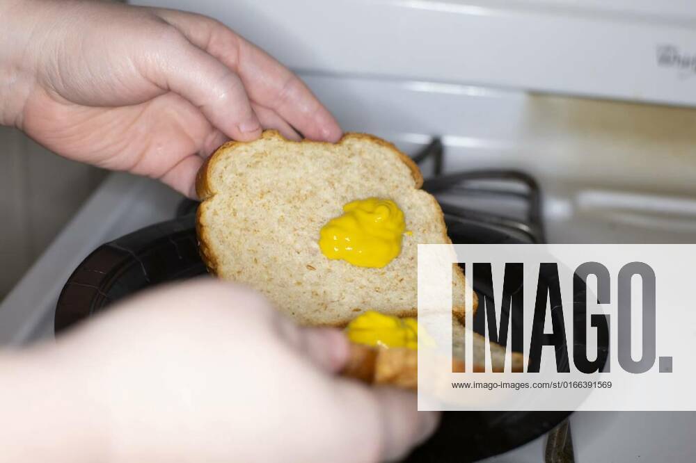Putting Mustard on a Sandwich, Preparing sandwich bread covered with clumps of mustard model released, Symbolfoto , 14.01.2021,