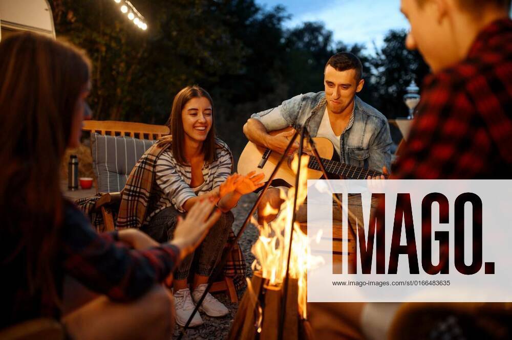 Friends playing on guitar by the bonfire, camping, Friends playing on guitar by the bonfire, picnic at camping in the forest. Youth having summer adventure on rv, camping-car on background. Two couples leisures, Friends playing on guitar by the bonfire, picnic at camping in the forest. Youth having summer adventure on rv, camping-car on background. Two couples leisures, 07.02.2021,