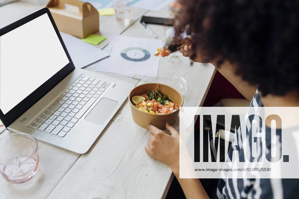 Businesswoman having poke bowl by laptop in lunch break at office model released, Symbolfoto property released, MEUF07121