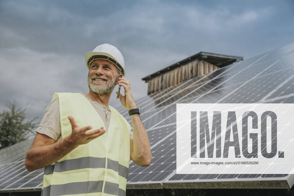 IMAGO Creative: Business, Innovative Technologie-Lösungen Engineer wearing hardhat talking on phone by solar panels model released, Symbolfoto, MFF09274