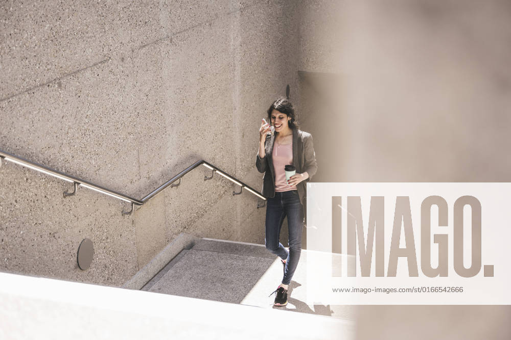 IMAGO Creative, Urban Lifestyle Smiling transgender woman talking on phone climbing steps of subway model released, Symbolfoto, UUF26885