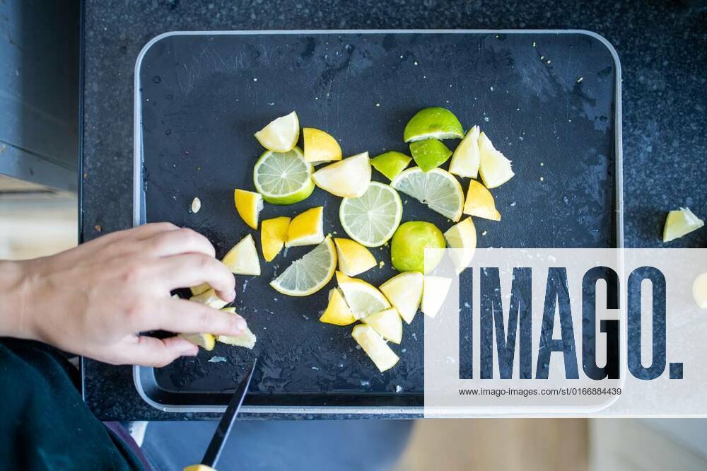 Female hands slicing lemons and limes on a black tray, Top view of female hands carefully slicing lemons and limes on black tray. Woman cutting citric fruit into small pieces forming a heart. Citrus drink preparation, 13.05.2021,