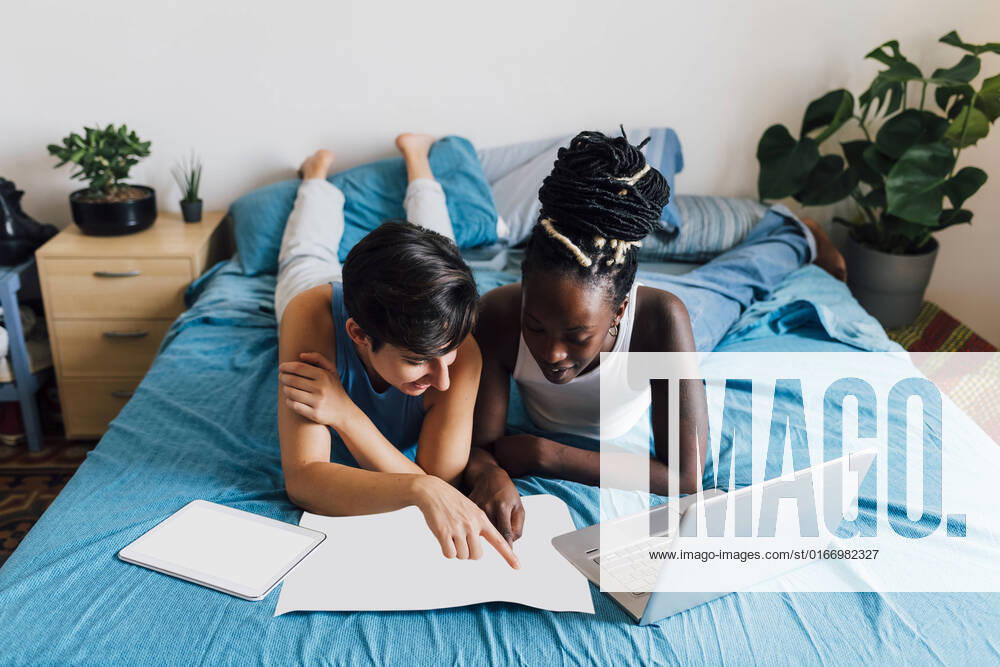 IMAGO Creative: Business, Innovative Technologie-Lösungen Lesbian couple with map planning trip lying on bed model released, Symbolfoto property released, MEUF07861