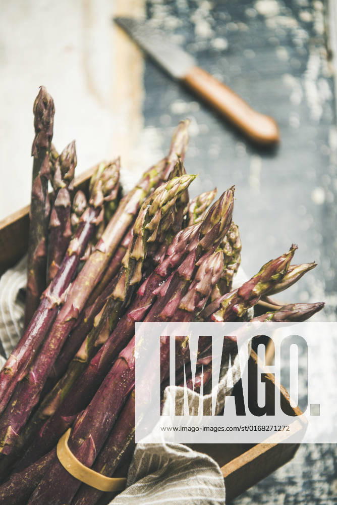 Fresh raw uncooked purple asparagus, selective focus Seasonal harvest produce. Fresh raw uncooked purple asparagus over wooden tray background, selective focus, vertical composition. Local market food concept