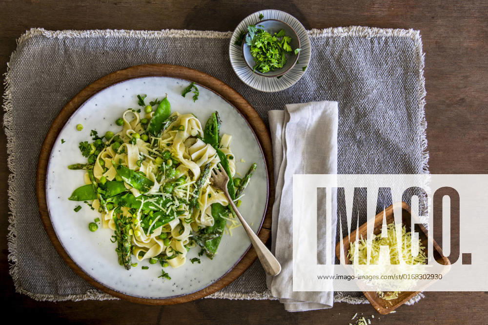 Freshly made Pasta Primavera with green asparagus, peas and sugar snaps on stoneware plate over wooden background with copy space