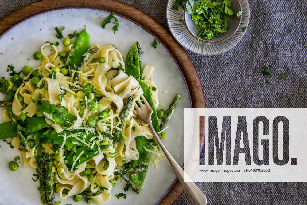 Freshly made Pasta Primavera with green asparagus, peas and sugar snaps on stoneware plate over linen place mat with copy space