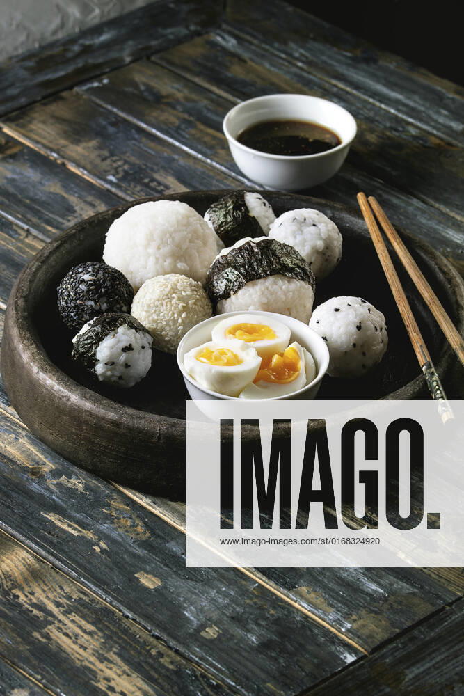 Rice balls and eggs Stone tray with different size rice balls with black sesame and seaweed nori, served with soft boiled eggs, soy sauce, chopsticks over wooden plank background. Asian style dinner.