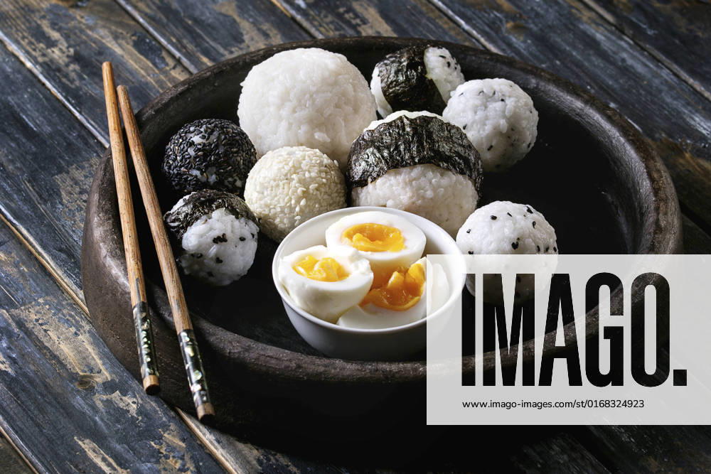 Rice balls and eggs Stone tray with different size rice balls with black sesame and seaweed nori, served with soft boiled eggs and chopsticks over wooden plank background. Asian style dinner.
