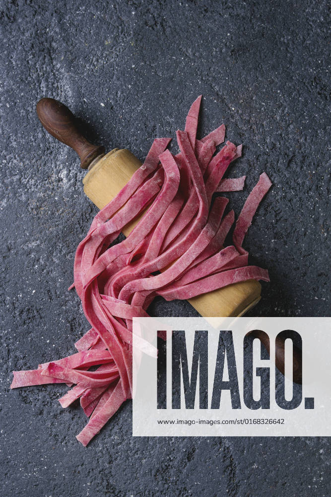 Fresh homemade pink pasta tagliatelle Fresh raw uncooked homemade pink beetroot pasta tagliatelle on wooden rolling pin over dark texture concrete background. Top view with space.