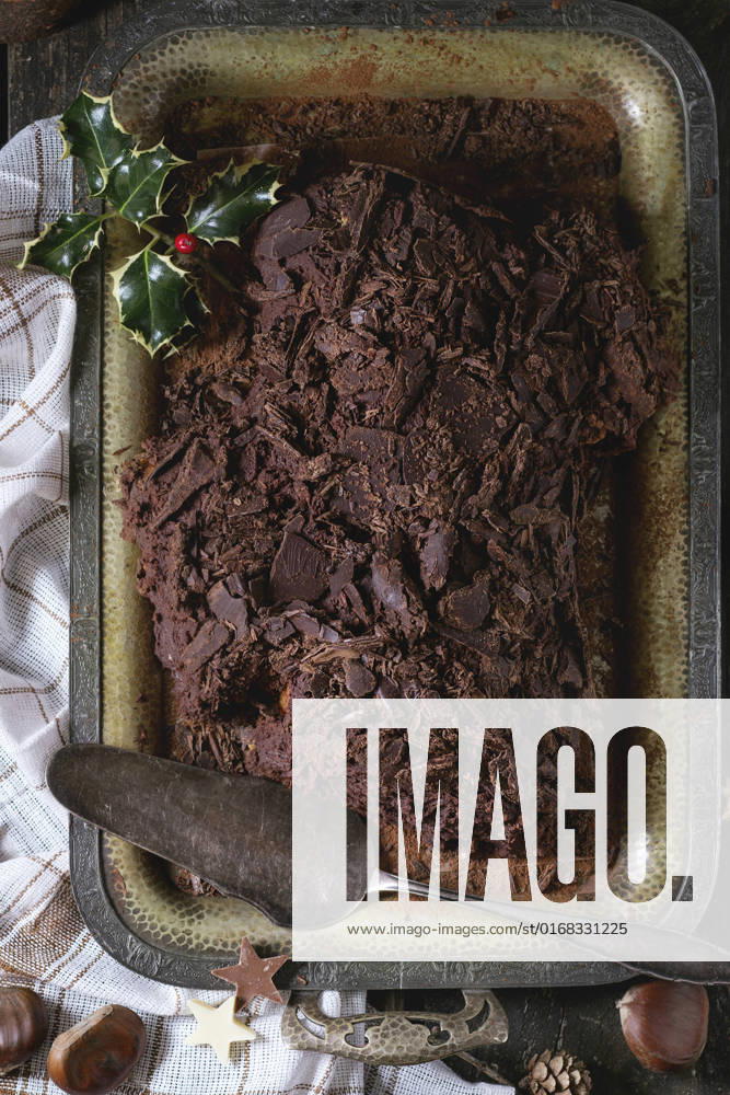Homemade christmas chocolate yule log Whole homemade Christmas chocolate yule log with chestnuts cream on vintage tray with white textile rag and chestnuts, chocolate stars and holly branch over old wooden table. Rustic style. Top view