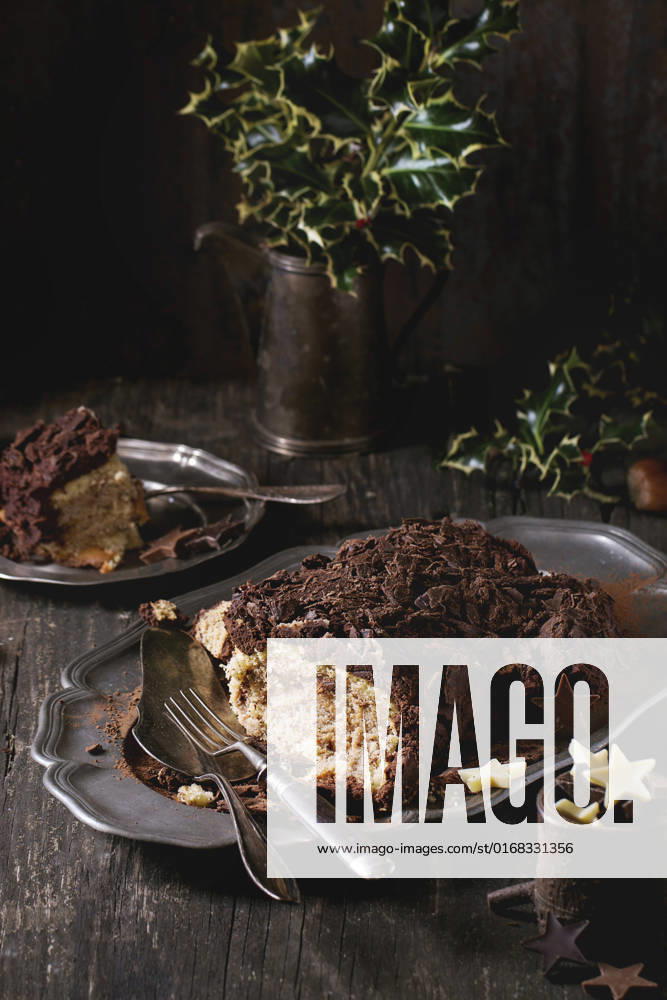 Sliced christmas chocolate yule log Sliced homemade Christmas chocolate yule log with chestnuts cream on vintage plate with forks, chocolate stars and holly branch over old wooden table. Dark rustic style.