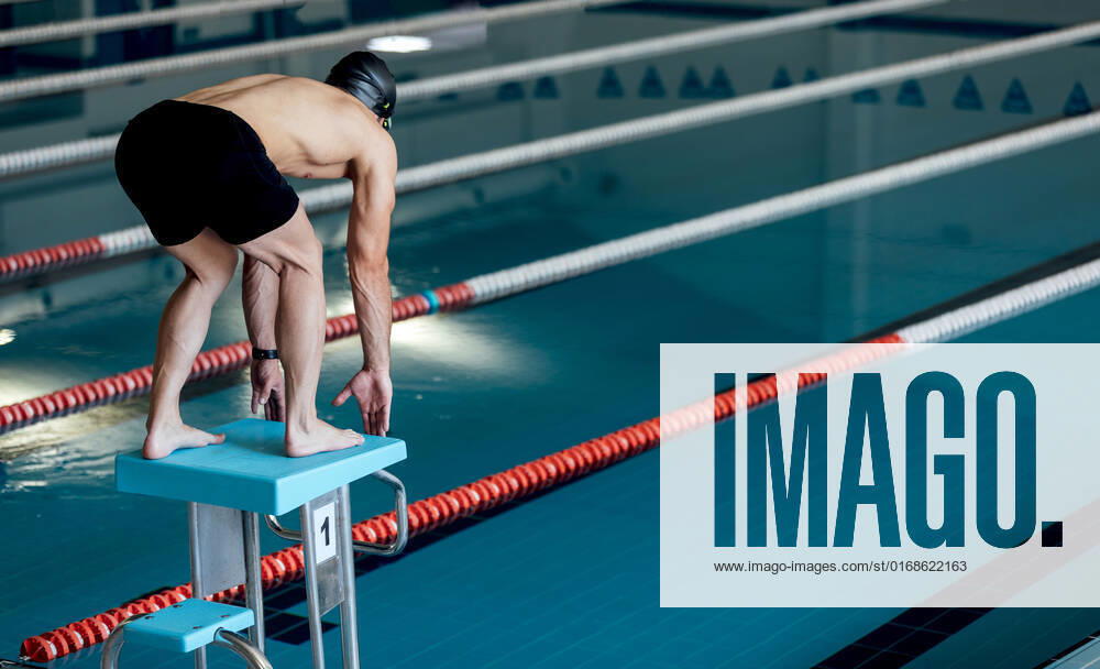 Back view of anonymous male athlete in swimming trunks leaning forward on starting platform over pool with floating markers, Model released SergioVictorVega_MaiquelSwimmer_7