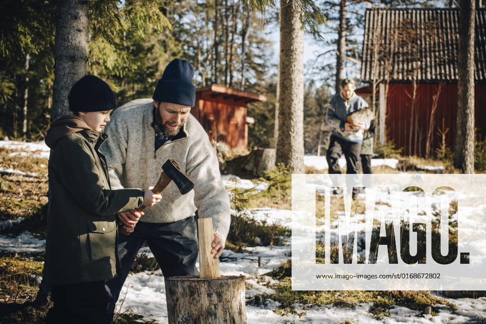 IMAGO Creative: Business - Work-Life Balance Father teaching son to cut log with axe in forest during winter Sweden, Stockholm, model released