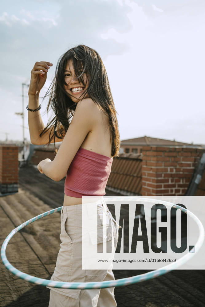 IMAGO Kreativ: Urbane Kultur - Sommer auf den Dächern Side view of cheerful woman spinning hoola hoop on rooftop Germany, Berlin, model released, property released