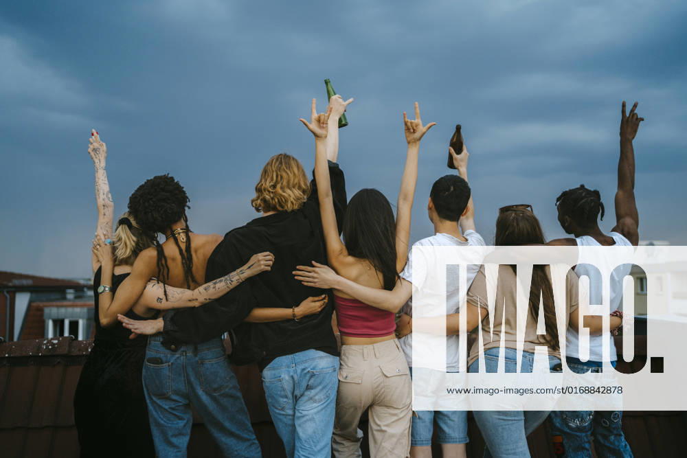 IMAGO Kreativ: Urbane Kultur - Sommer auf den Dächern Rear view of multiracial young men and women gesturing with arms raised on rooftop at dusk Germany, Berlin, model released, property released